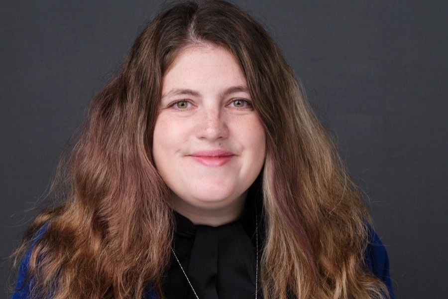 young woman in black sweater smiling against black background